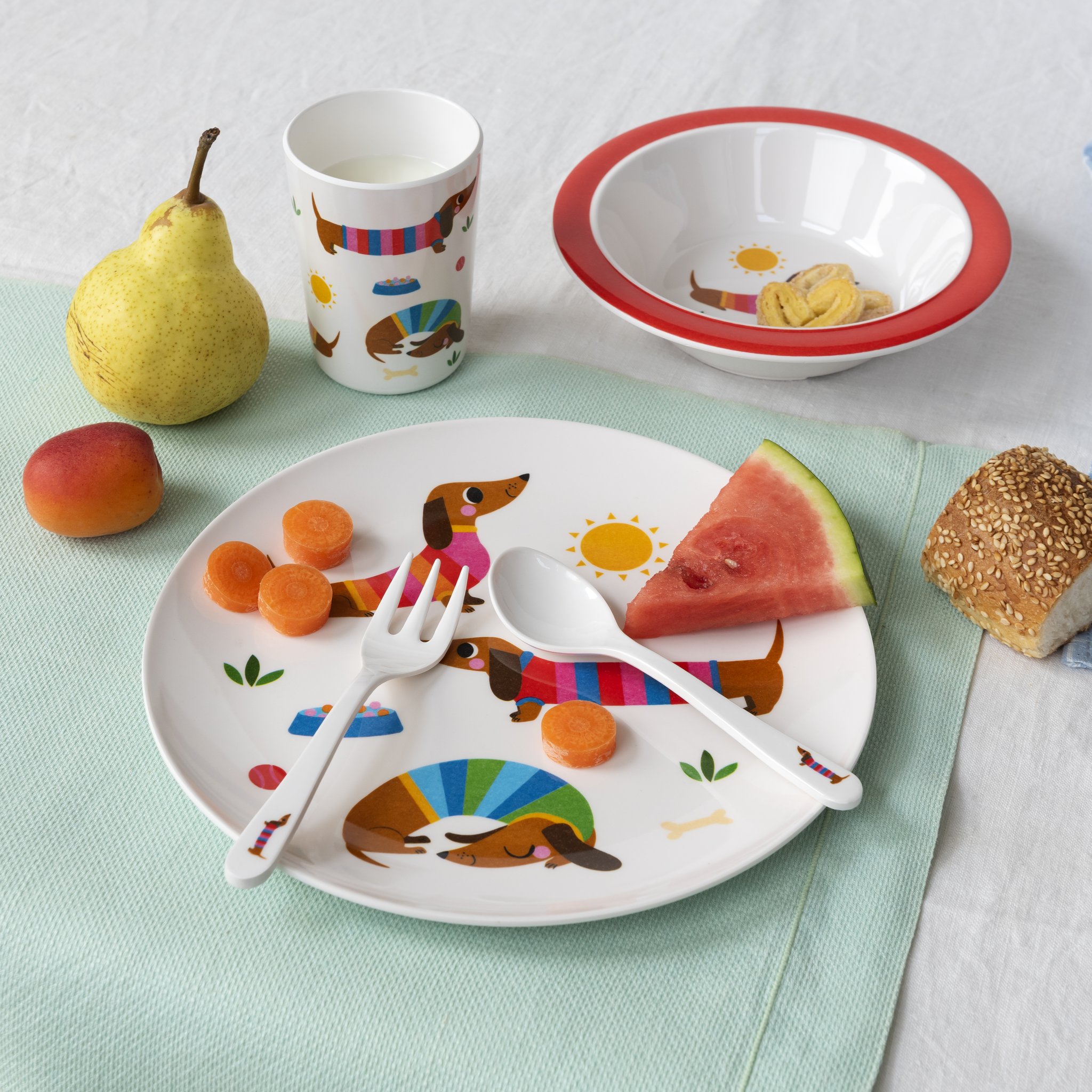 Set pappa bambini bassotto apparecchiato con frutta, panino e melone sul tavolo
