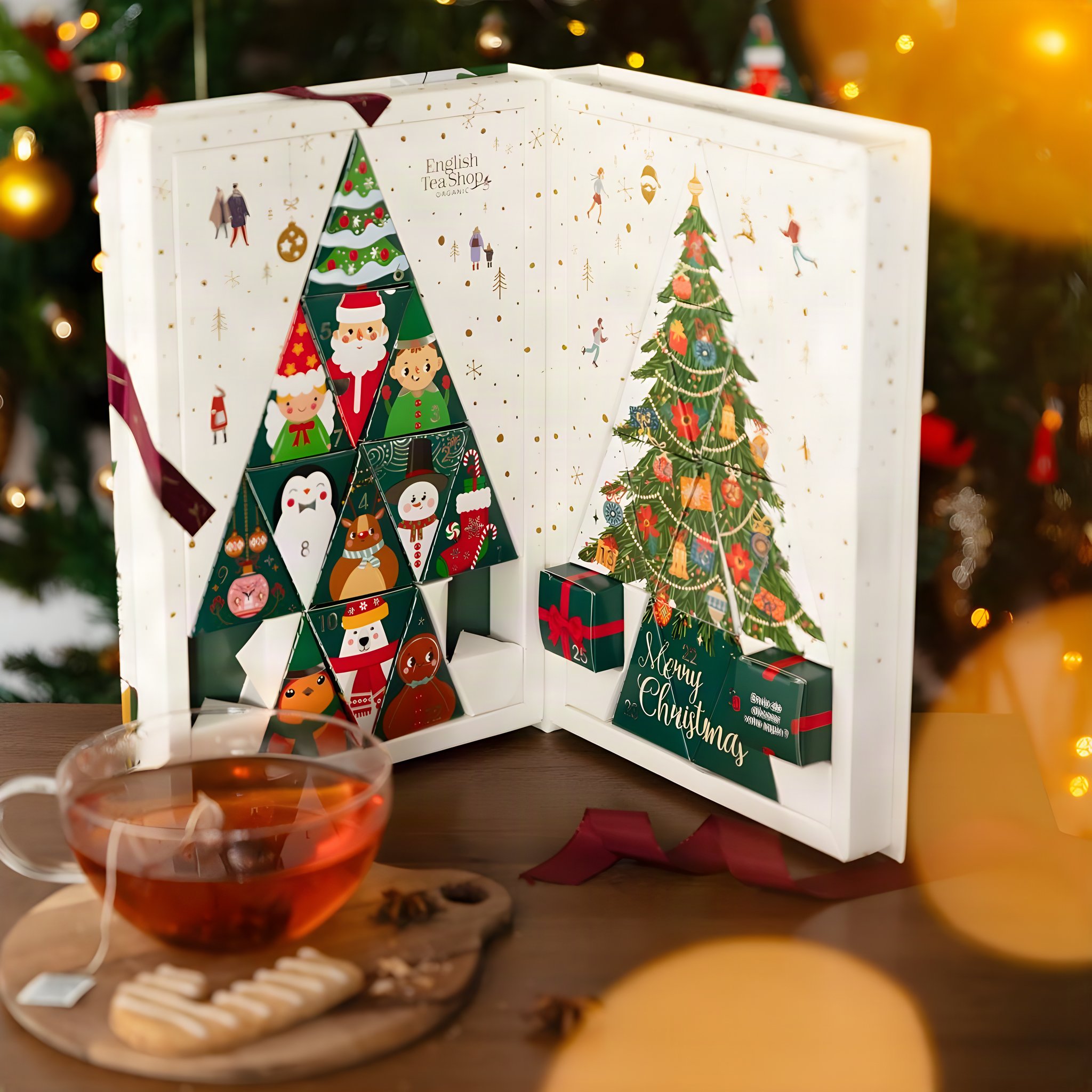 Opened Christmas tree tea advent calendar on a table beside a cup of tea and biscuits