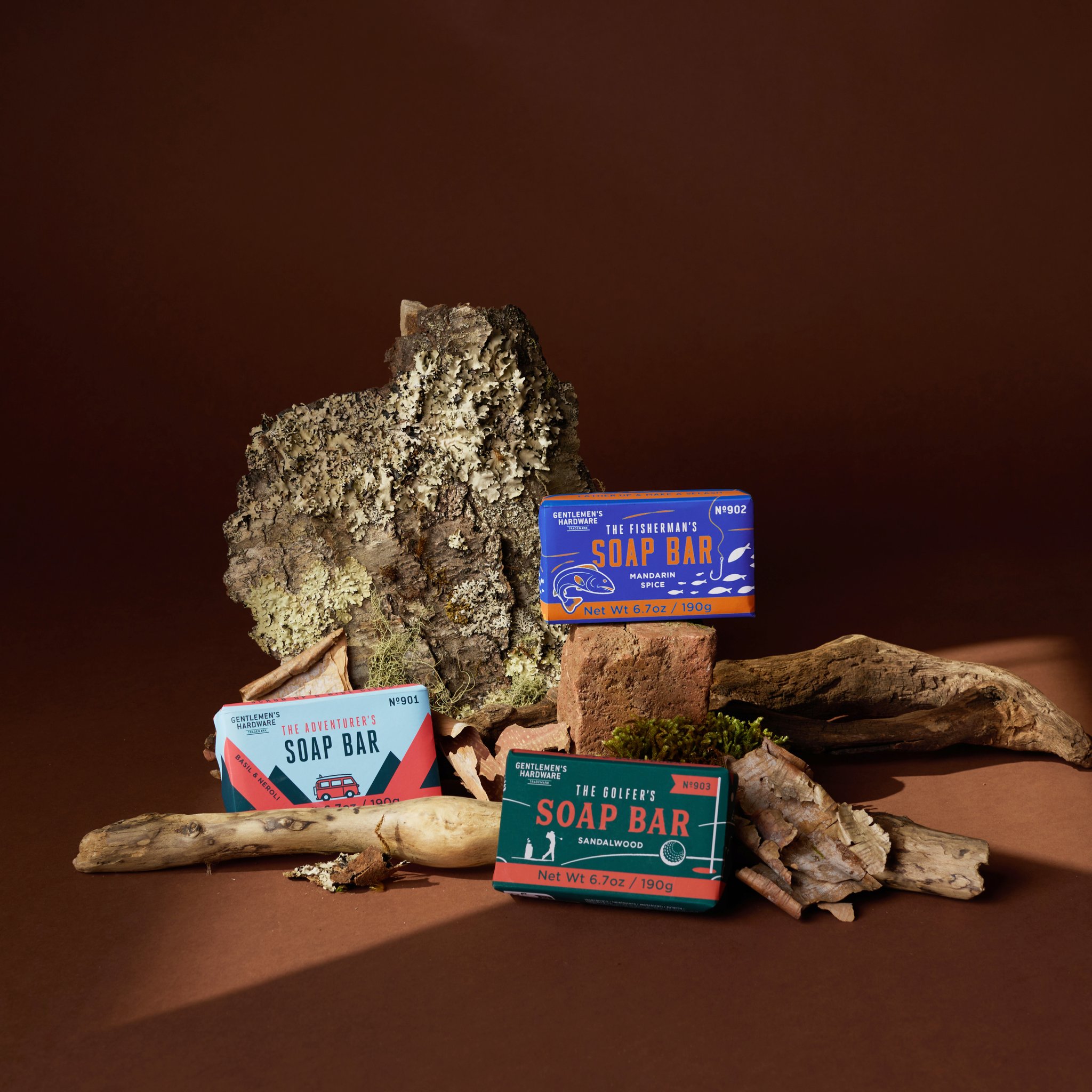 Die Abenteurer-Seife mit Fischer- und Golfer-Seife zwischen Rinde, Moos und Treibholz vor braunem Grund