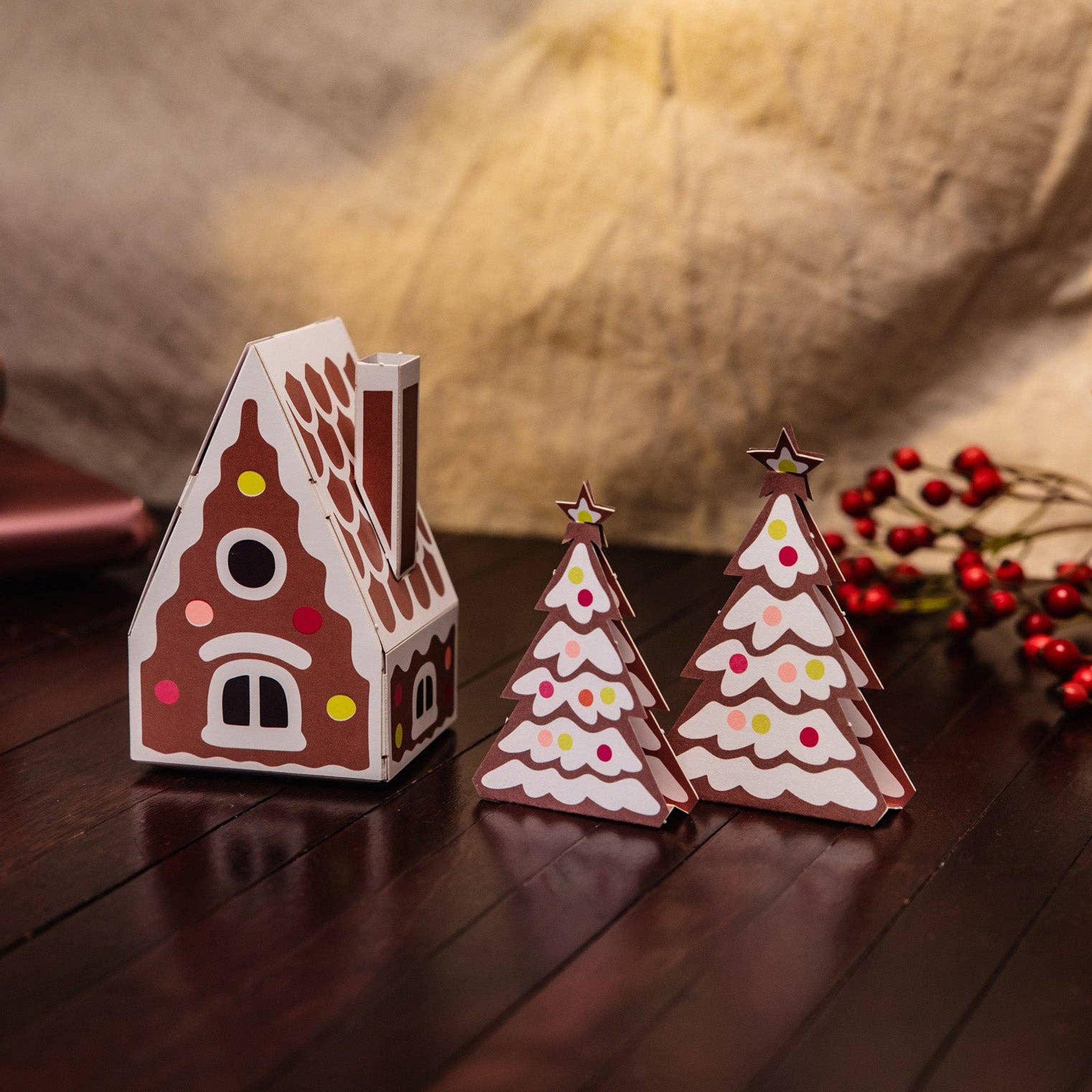 Papier-Lebkuchenhaus mit Tannenbäumen als Adventsdeko auf dem Holztisch