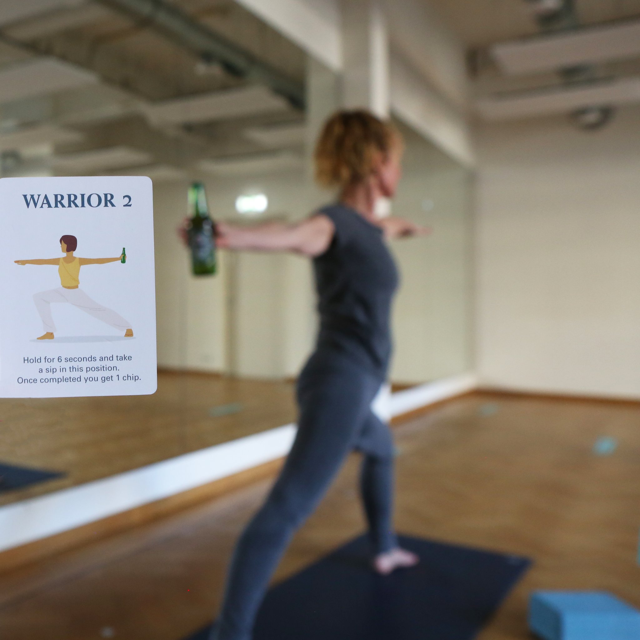 Frau in der Krieger-Pose mit Bierflasche, Karte «Warrior 2» daneben