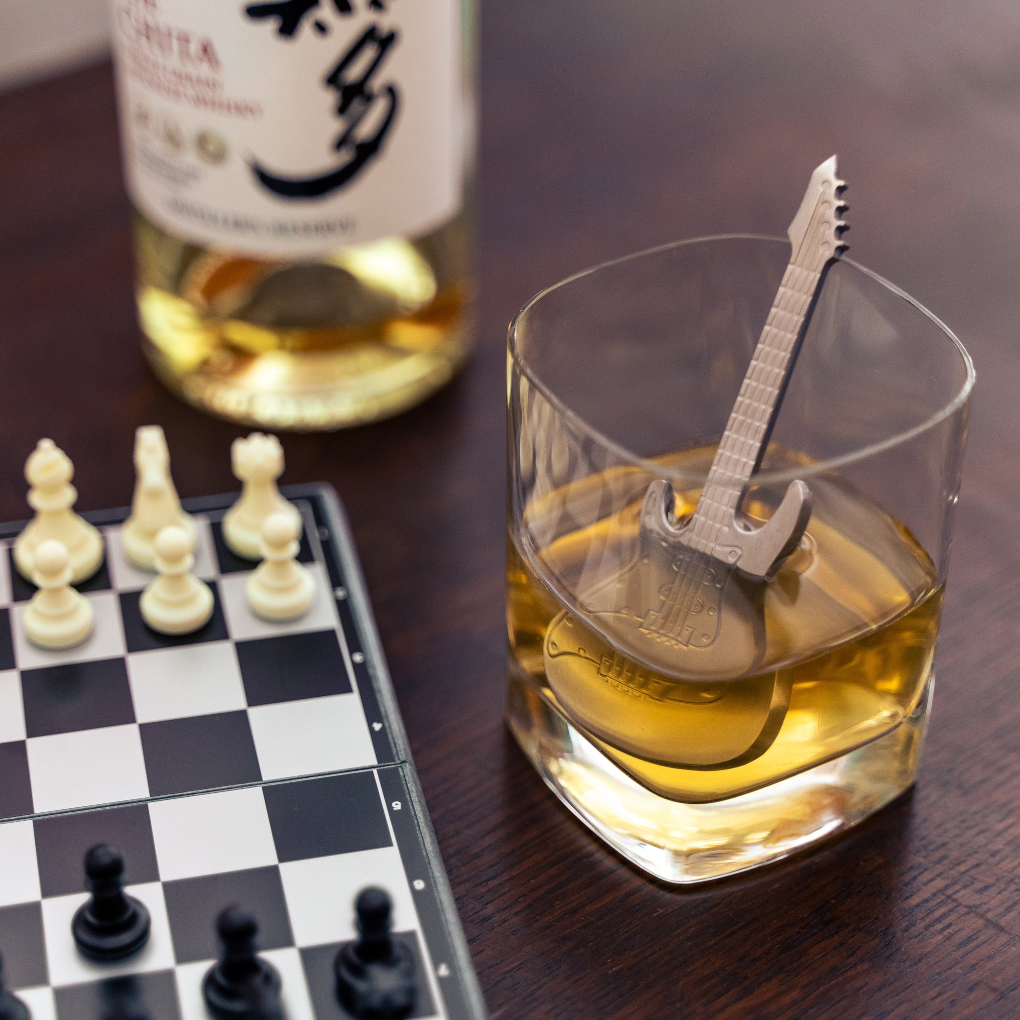 Refroidisseur guitare en acier inoxydable dans un verre à whisky sur l'échiquier