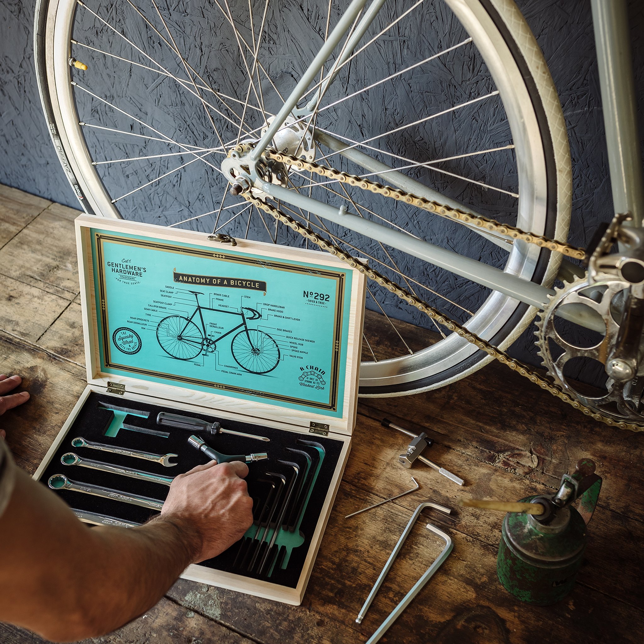 Hand greift in die offene Holzkiste neben einem Rennrad, Schraubenschlüssel und Inbusschlüssel liegen auf der Werkbank