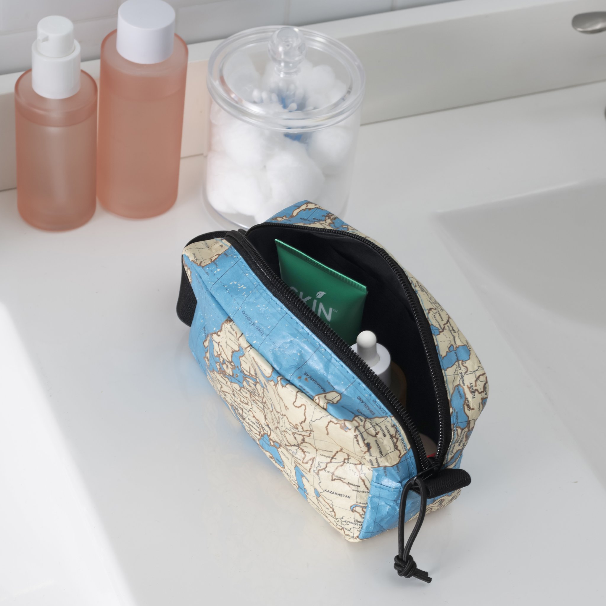 Offene Kulturtasche mit Weltkarten-Muster auf dem Badezimmer-Waschtisch