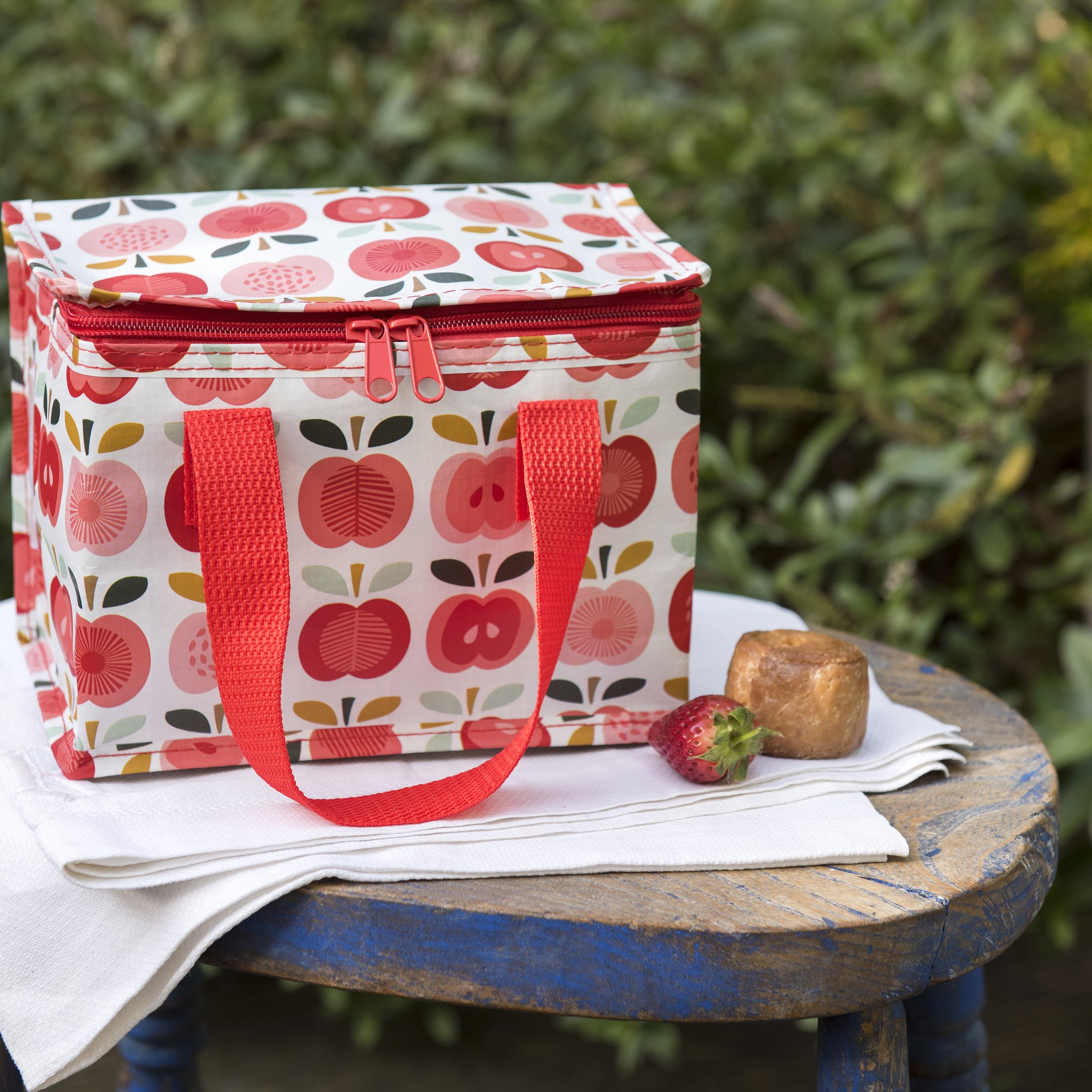 Apfel-Kühltasche auf einem Holzhocker im Garten, daneben Erdbeeren