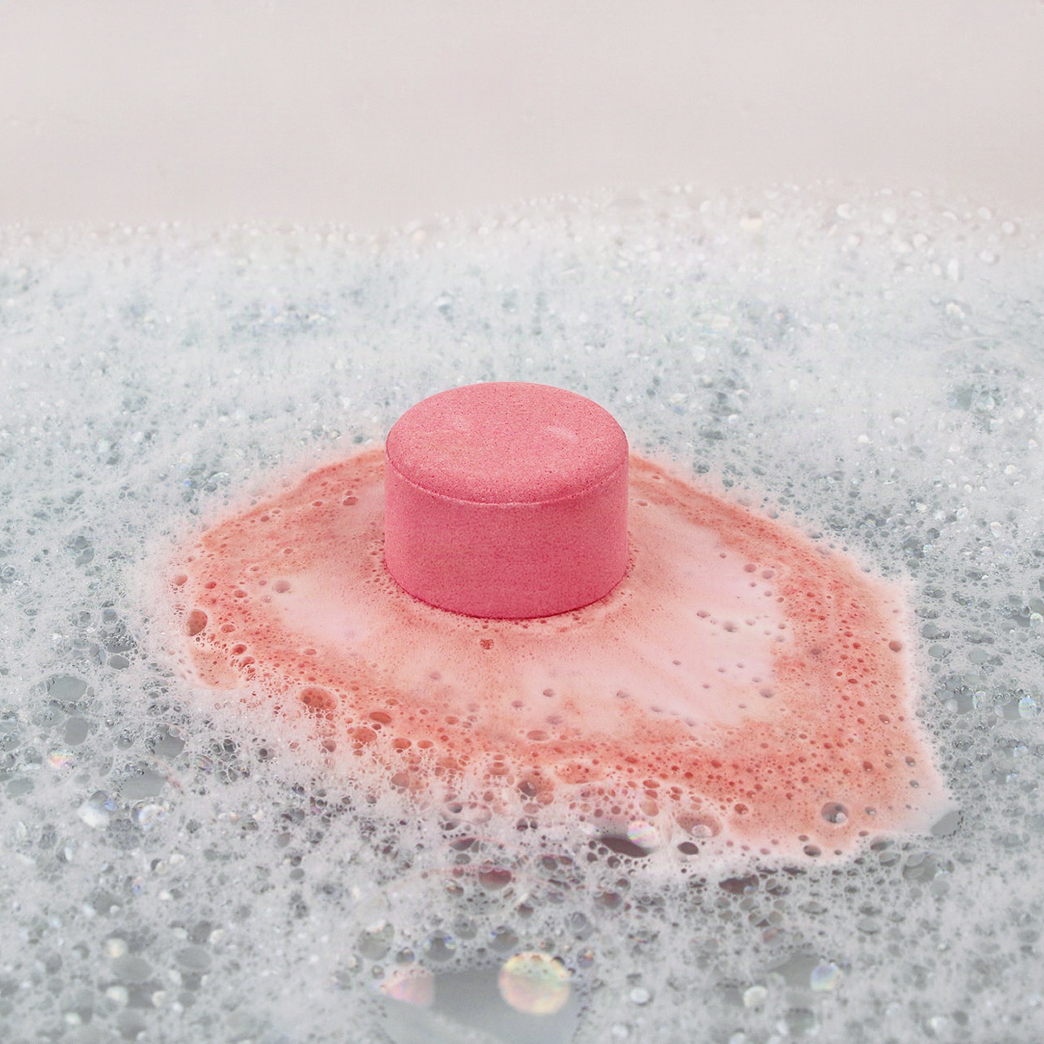 Pink marshmallow bath bomb fizzing in the bath water and turning the foam pink