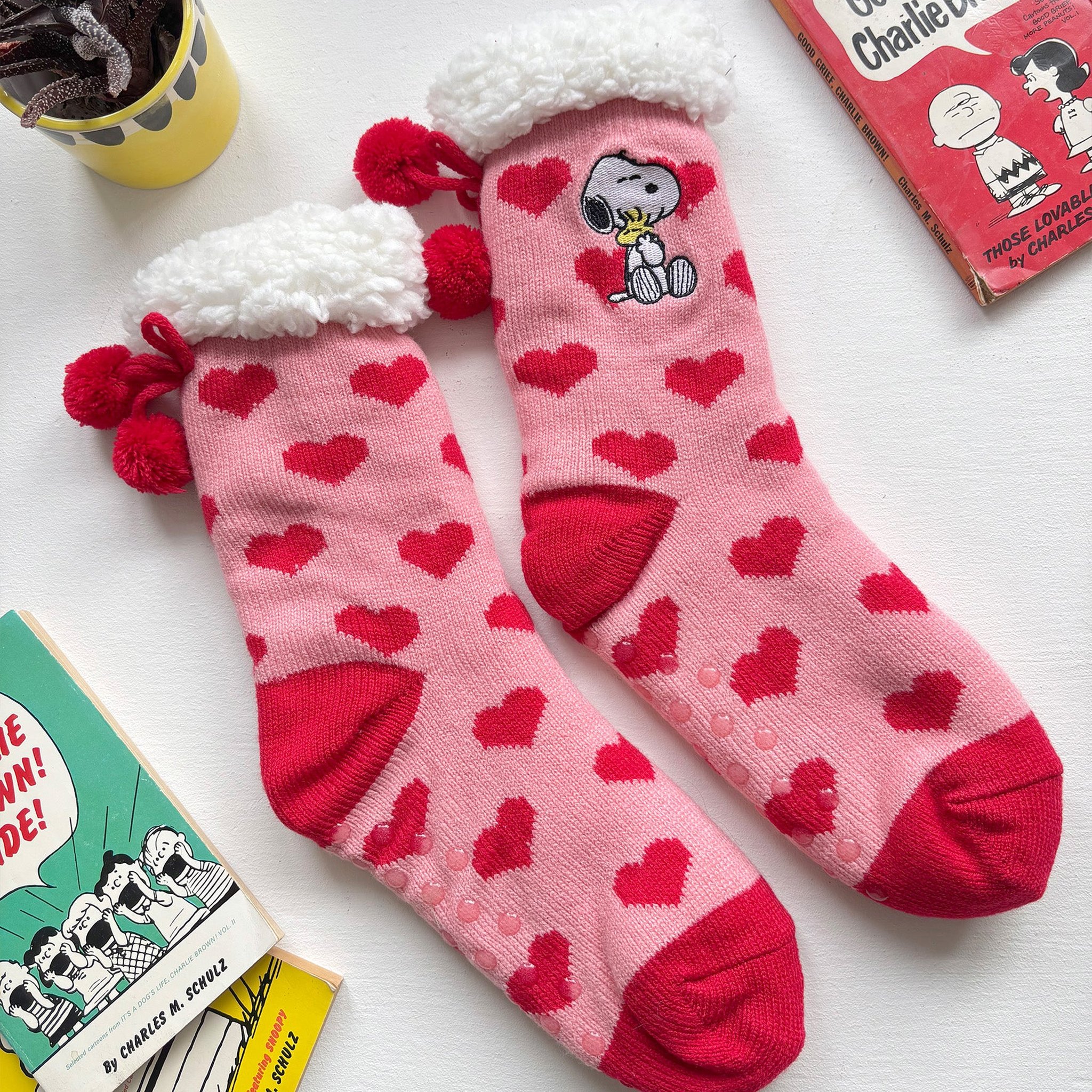 Snoopy Love Kuschelsocken mit Bommeln neben Peanuts-Büchern