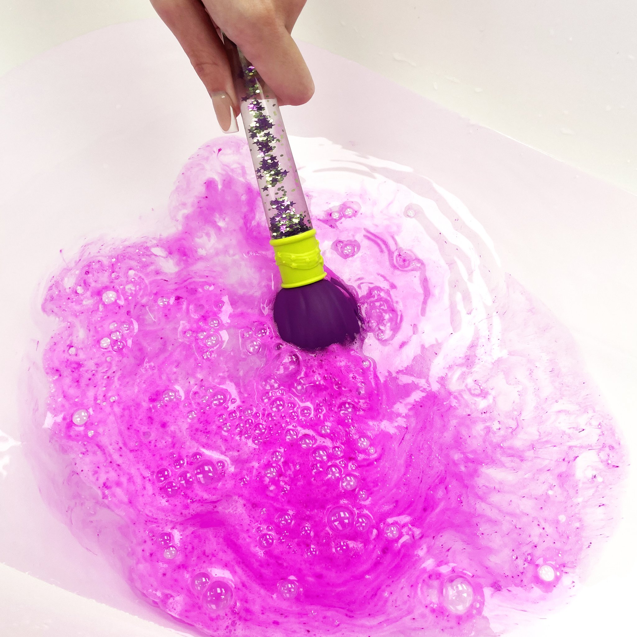 Brush with bath bomb painting pink foam in the water