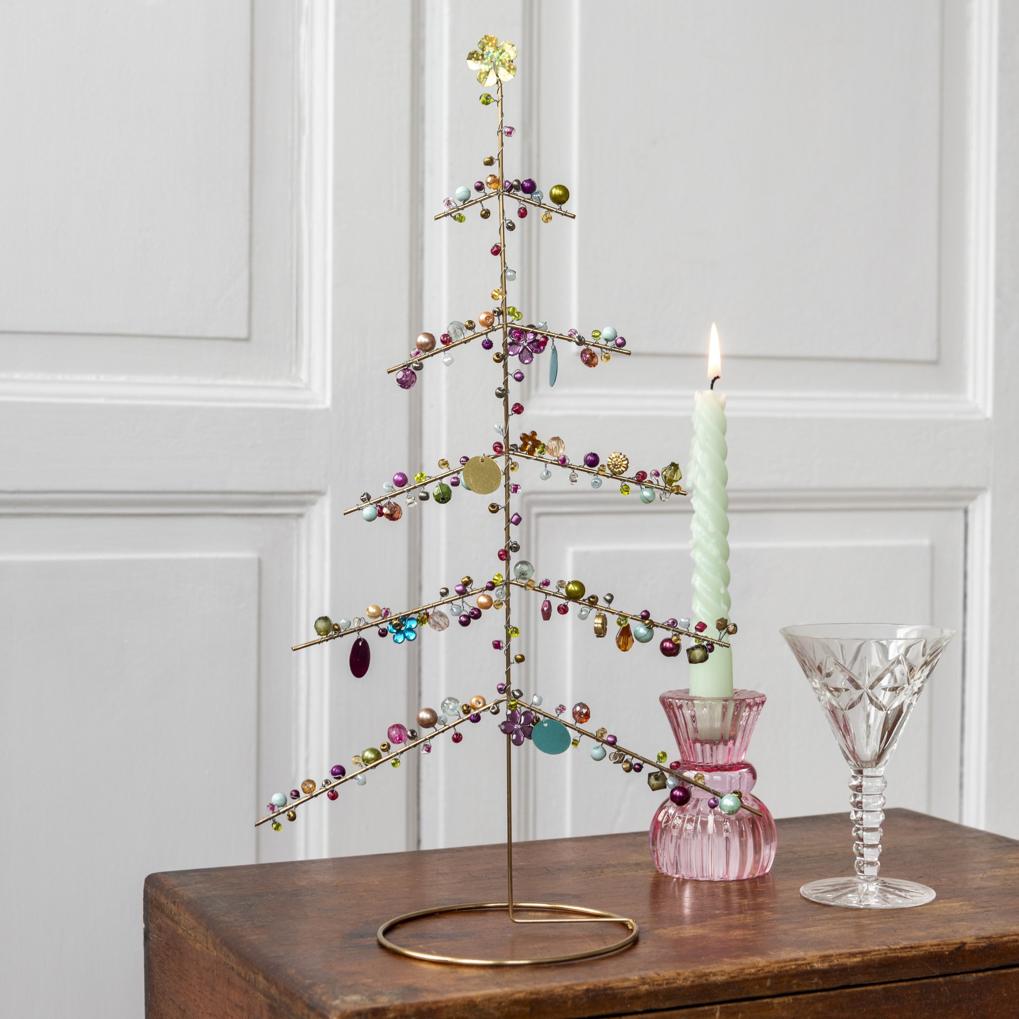 Albero di Natale in filo metallico con perline sul comò accanto a candela e bicchiere
