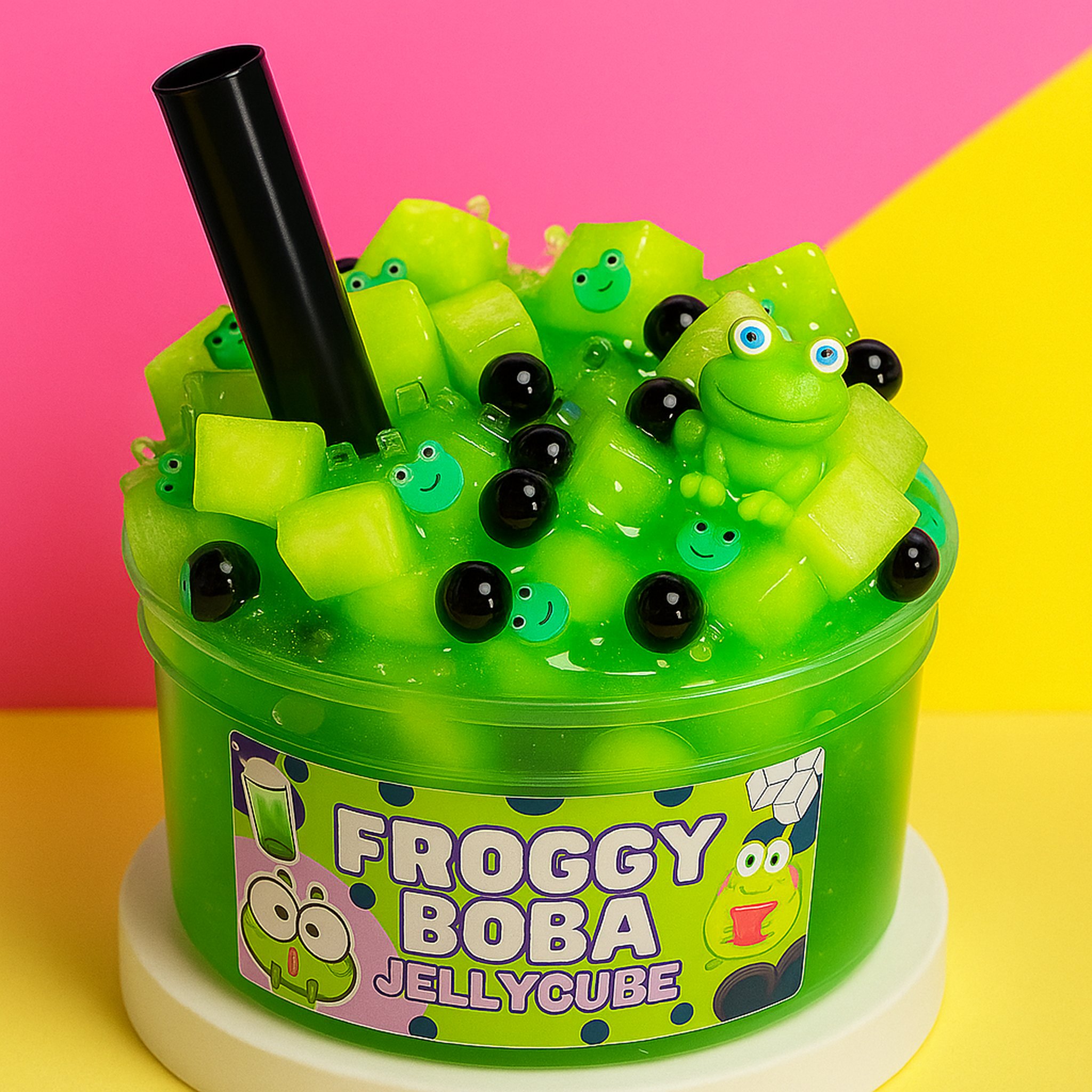 Froggy Boba Jelly-Cube-Slime mit Strohhalm vor pink-gelbem Hintergrund (KI-Darstellung)