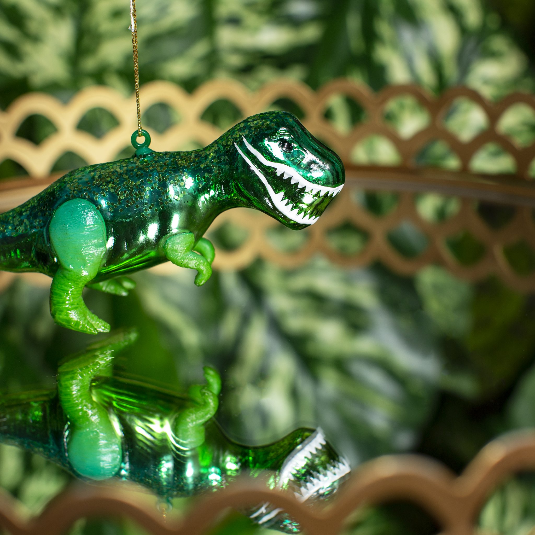 Décoration de sapin T-Rex Sass & Belle, dinosaure vert en verre devant des branches de sapin