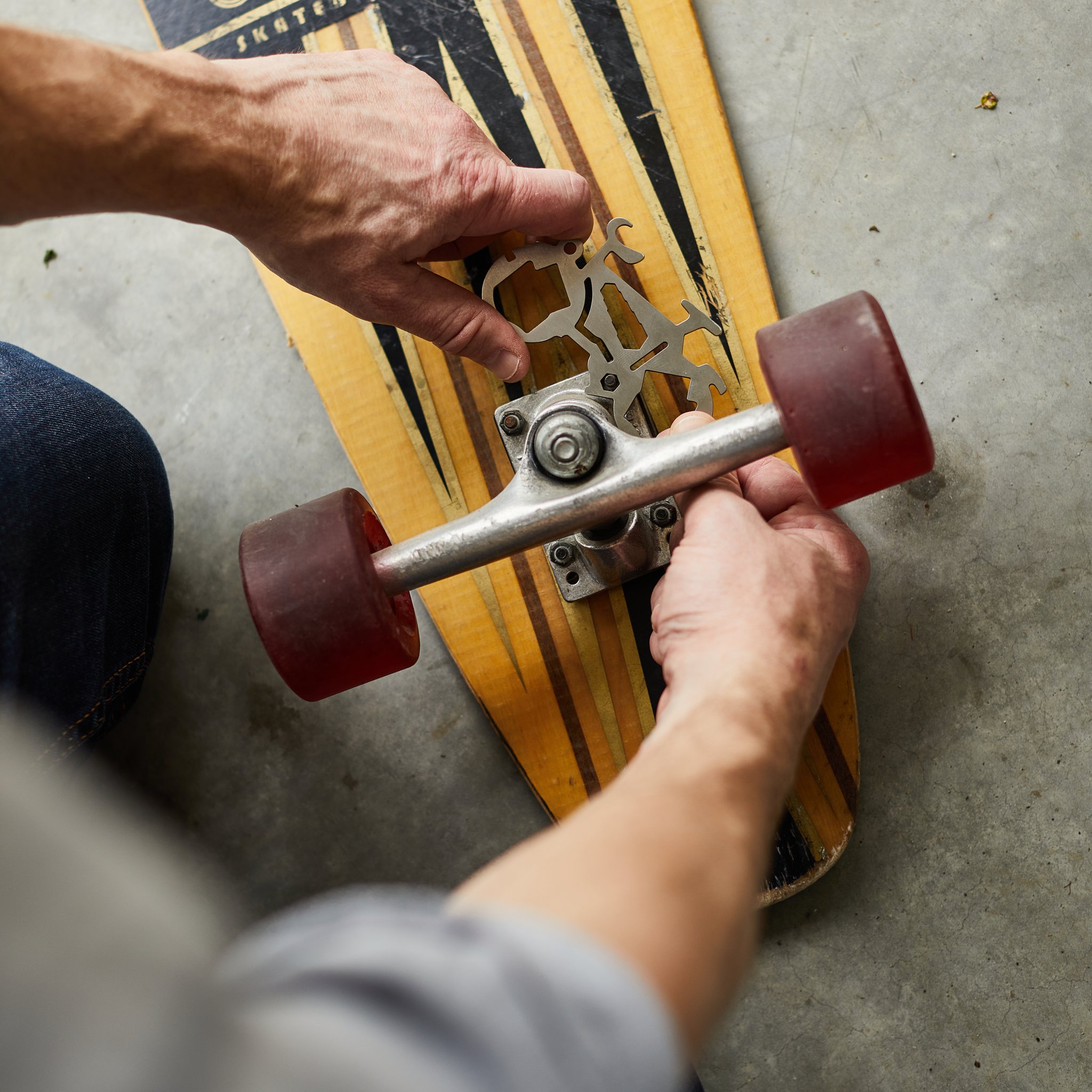 Person applying the Mini Bicycle Multi-Tool to a skateboard truck nut, with red wheels either side