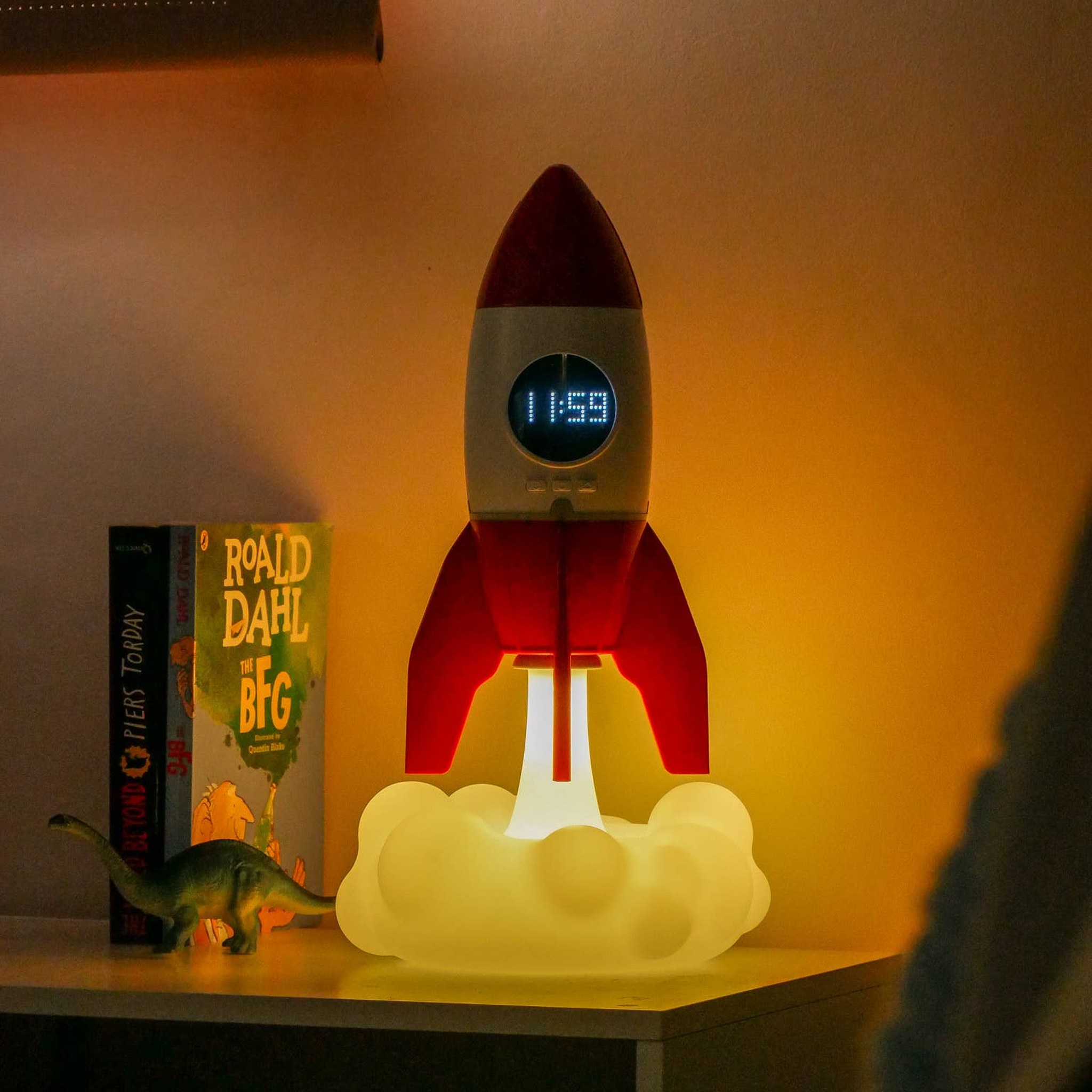 Rocket night light on a bedside table, the cloud glowing warm, the clock at 11:59