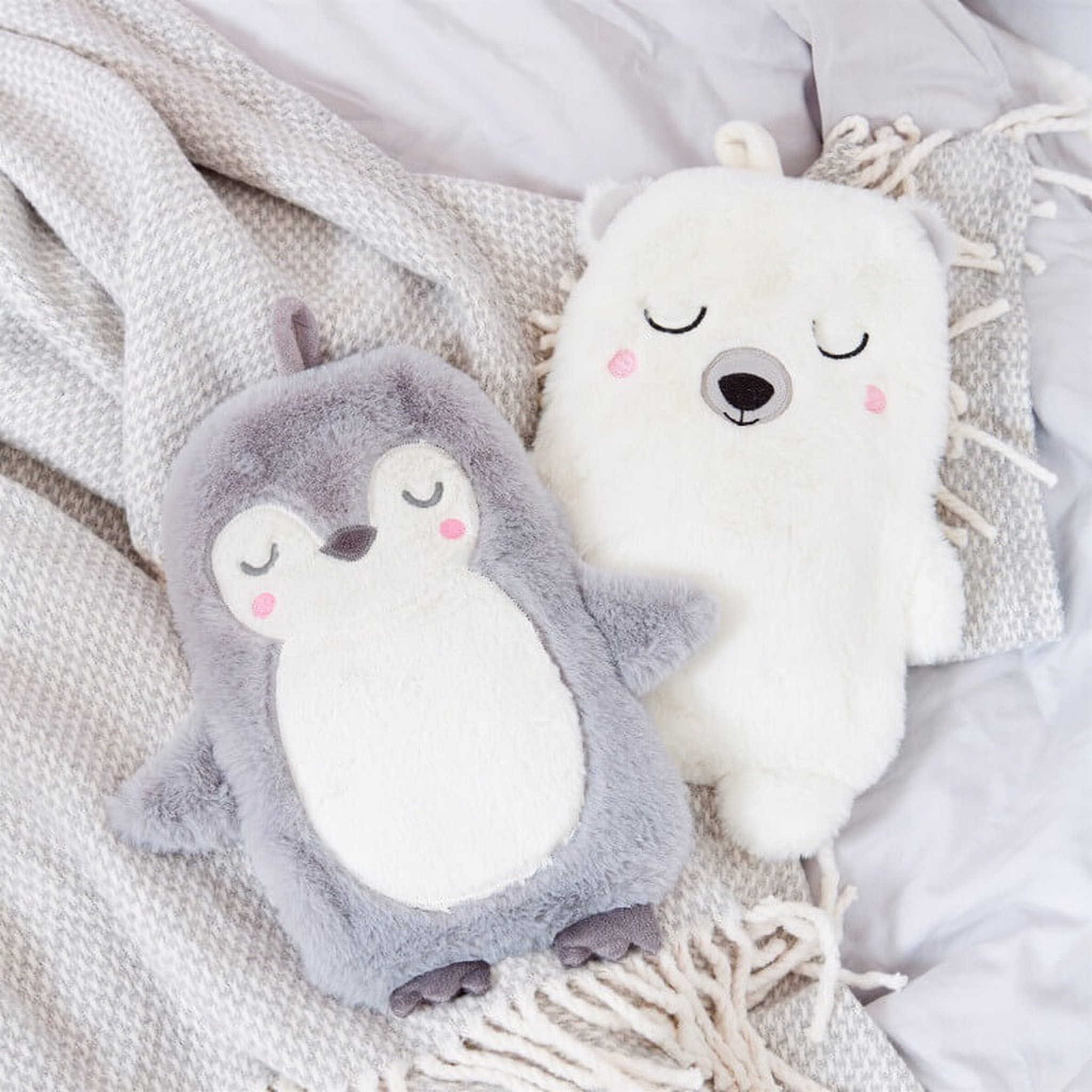Wärmflasche Eisbär Nanook von Sass & Belle neben der Pinguin-Wärmflasche auf grauer Decke