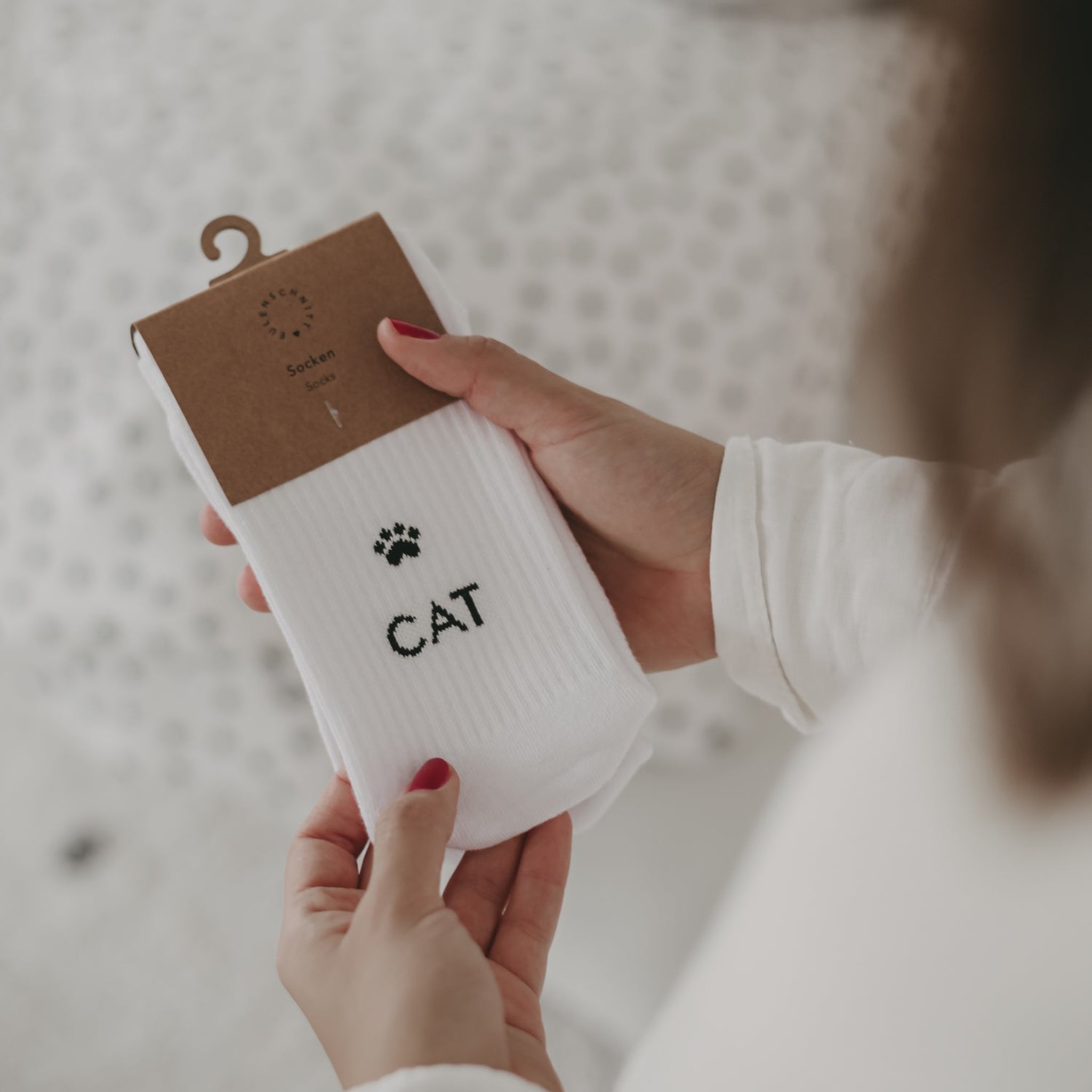 Hände halten die Socke mit Schriftzug CAT und Pfote an einem Kartonaufhänger