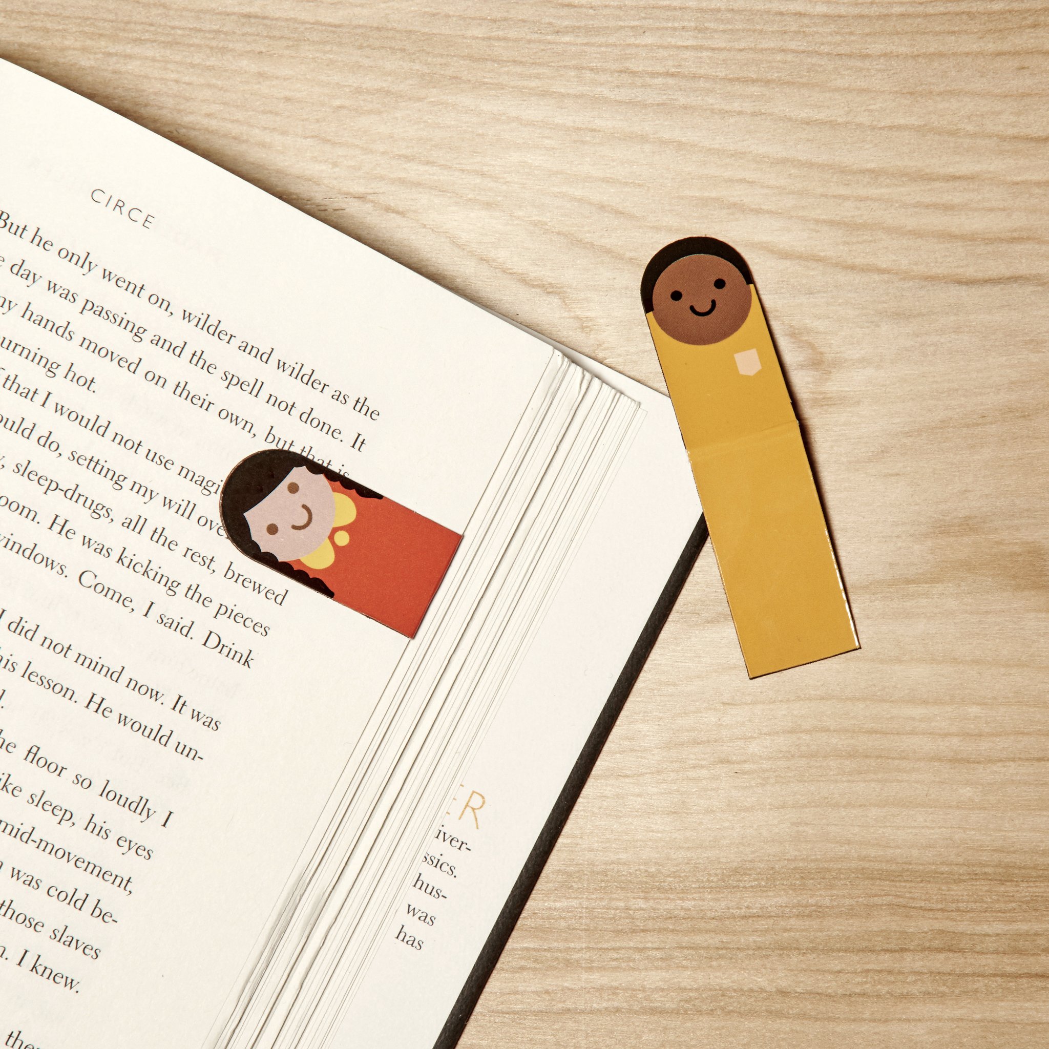 Magnetisches Lesezeichen mit Figur klemmt an der Buchseite, zweites liegt daneben