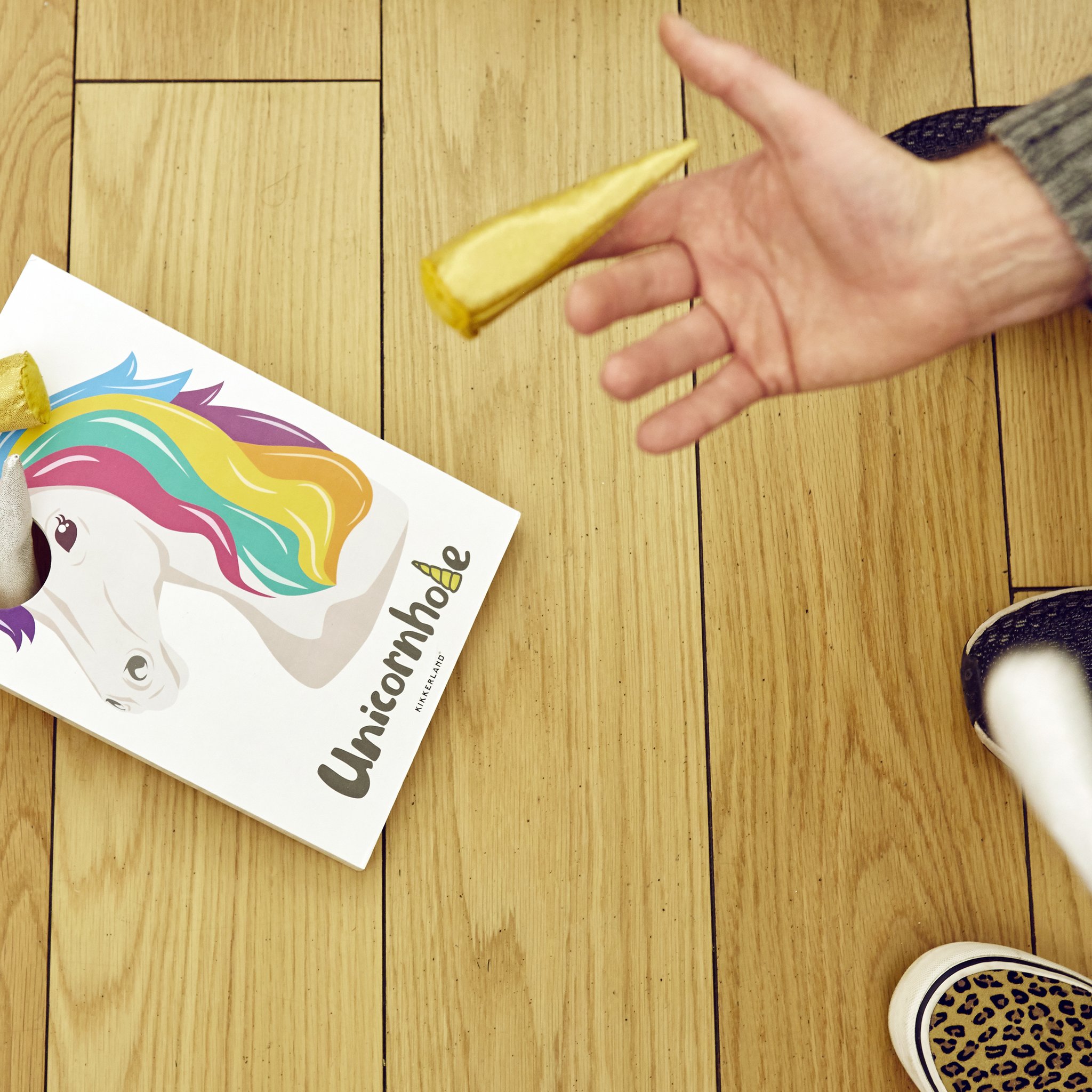 Main lançant une corne pailletée sur le plateau Unicornhole au sol
