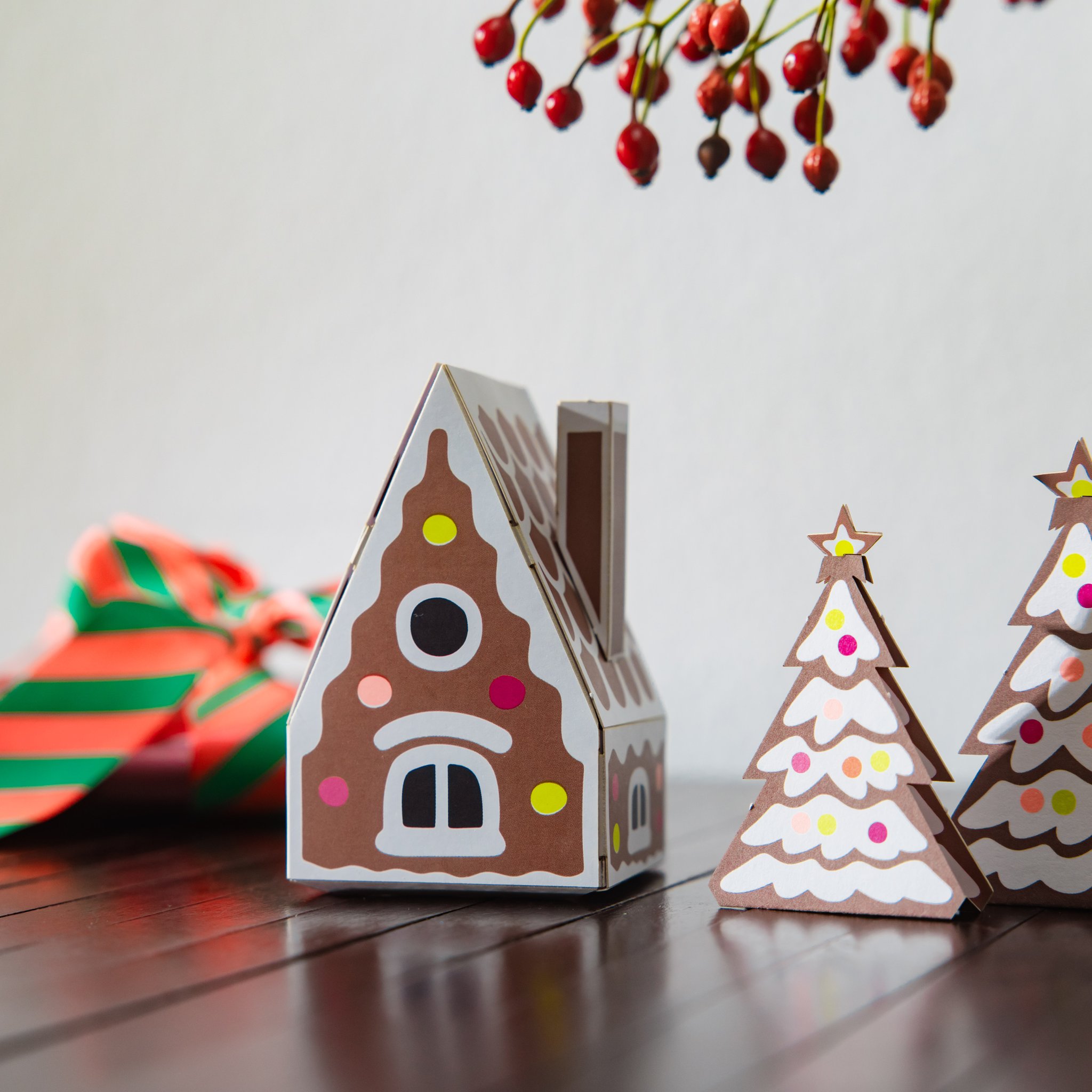 Gebasteltes Lebkuchenhaus aus Papier mit Tannenbäumen und Geschenkband auf dem Tisch
