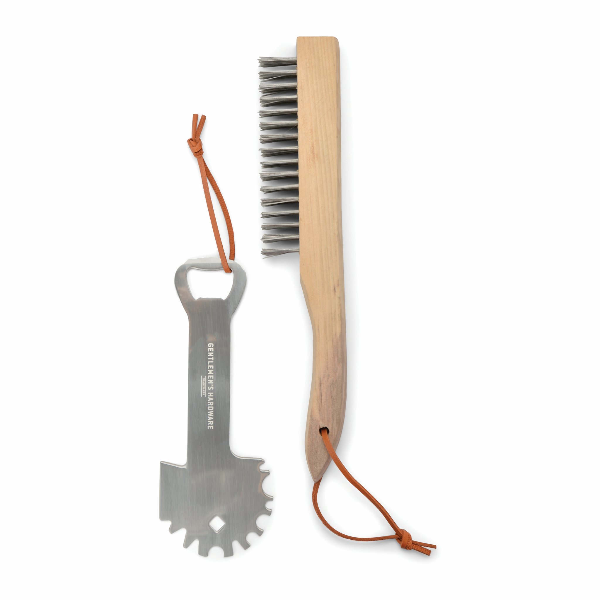 Grattoir avec décapsuleur à côté de la brosse métallique du kit pour l'entretien du barbecue, sur fond blanc